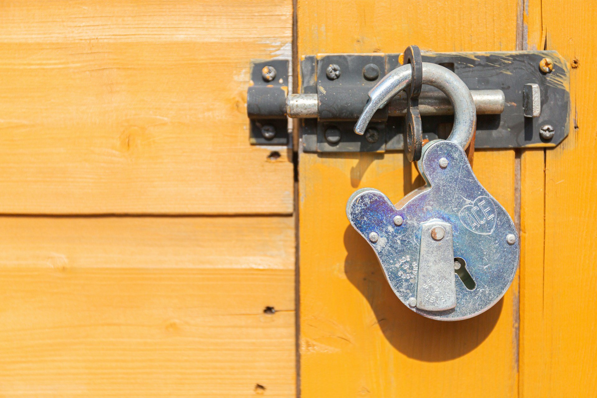 A brown wooden door with a single silver padlock